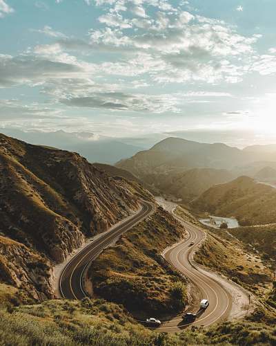 dirt road road in between hill under white clouds and blue sky gravel